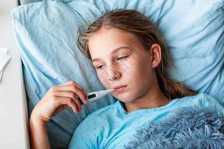 患有高发烧和头痛患病的十几岁少女躺在床上 将温度计放在嘴里温度童年保健毯子卫生枕头感染说谎病人孩子女孩高清图片素材