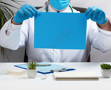 身穿白色医疗大衣的医生坐在棕色的桌子上工作蓝色处方办公室药品治疗工作室手套临床男人空白的高清图片素材