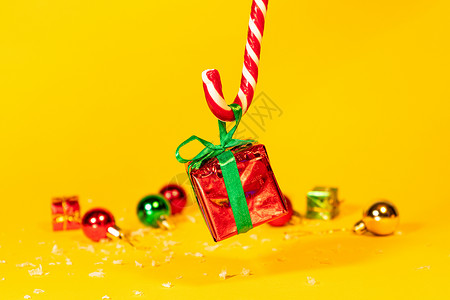 圣诞装饰手杖糖糖果手杖棒棒糖拿着一个礼盒 里面有黄色背景的圣诞礼物 圣诞糖果和新年装饰食物薄荷展示盒子礼物季节装饰品庆典甘蔗传统背景