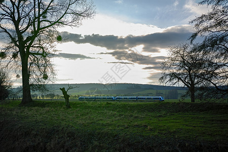 一辆移动的现代区域列车 在一片绿地和阴云的天空中高清图片