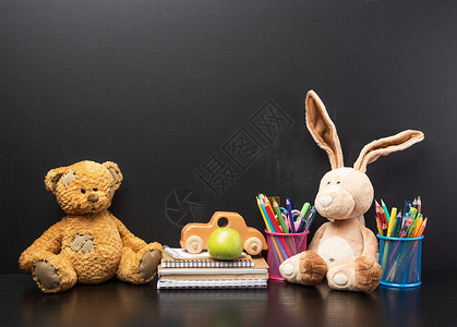 叼着铅笔的兔子坐在空黑粉笔板背景上的棕色泰迪熊文具和棕色泰迪熊背景