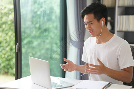 亚洲年轻学生男性企业家戴着耳机通过视频电话会议在家学习在线学习 电子学习网络研讨会会议 covid大流行中的社会距离商务互联网人背景图片