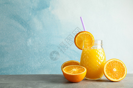 灰色桌子上装有新鲜橙汁 小管和橙子的玻璃罐 背景为彩色 文字空间 新鲜天然饮品情调作品饮料食物饮食木板榨汁机异国排毒水果背景图片