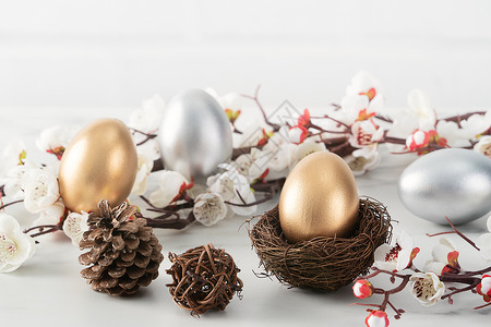 洒金金蛋金蛋和银色复活节鸡蛋 在巢中与白梅花装饰假期李子风格木头桌子季节卡片礼物乐趣背景