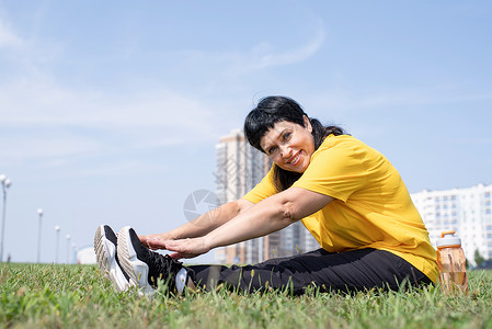 高级女性在公园的草地上拉长双腿 在城市背景上伸展老年微笑运动女士退休锻炼运动装福利力量活动背景图片