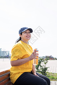 在运动场户外锻炼后 对高龄妇女饮用水进行微笑白色公园运动装黄色成人运动老年健康摇床闲暇背景图片