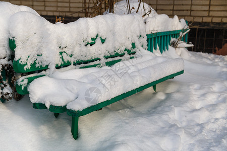 冬天绿色靠近公寓大楼入口处的绿色长椅 冬季日光下满层厚厚雪背景