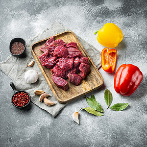 餐桌上新鲜牛肉块 配有准备做饭的原料 用白石底 方形灰色岩面上的甜辣椒背景图片
