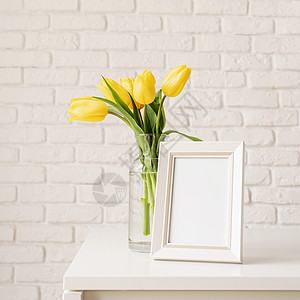 玻璃花瓶中的黄色郁金香和白砖墙背景上的空白照片框花瓣礼物叶子植物框架桌子花朵季节庆典花束背景图片