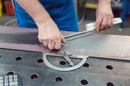 使用折叠规则计量钢条的金属工人金工机械蓝色职场生产工业制造业项目铁匠职业背景图片