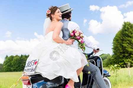 自行车上恋人刚结婚 在摩托摩托车上结了婚帽子女士夫妻发动机花束小路乡村公园驾驶新郎背景