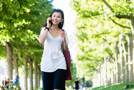 在公园中行走的清廉的年轻女子黑发娱乐太阳镜叶子女性植被长廊长发游客配件背景图片