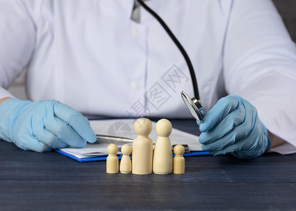 一名穿白色大衣的医生坐在一张桌子和一些家庭木头人物席上诊所高清图片素材