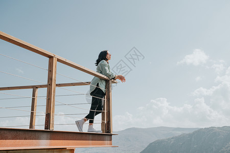 在一条大河和群山的阳台上 女人在阳光明媚的日子里过着自由和自由的概念 健康天堂耀斑娱乐地球微风女士房间信仰思维射线背景图片