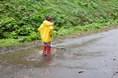 雨坑玩耍的女孩穿着黄色雨衣 同时在降雨时跳上水坑孩子外套季节快乐童年衣服乐趣雨滴幸福天气背景