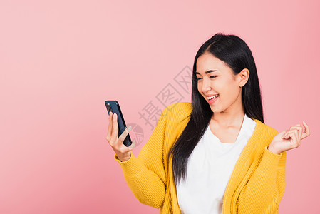 粉色电话快乐的亚洲肖像 美丽的可爱可爱年轻女子 兴奋地笑着拿着手机乐趣女士女孩胜利手势短信优胜者工具电话技术背景