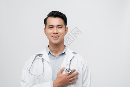 英俊的年轻医生在孤立的背景中戴着听诊器 手放在胸前微笑 面露感恩的手势 健康概念种类高清图片素材