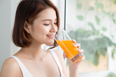 年轻快乐的女子 喝橙汁 站在窗户旁边头发水果微笑饮食玻璃女士早餐饮料果汁橙子人们高清图片素材