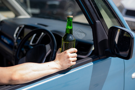 跪着罪犯一个不露面的女人一边开车一边喝着一瓶啤酒 驾驶时违法和饮酒背景