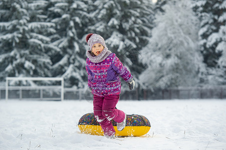 玩雪的小姑娘一个冬天的小女孩 穿着紫色衣服和一个充气圈 在一片雪覆盖的森林里走在街上帽子微笑雪花季节游戏孩子女孩小姑娘圣诞礼物圆圈背景