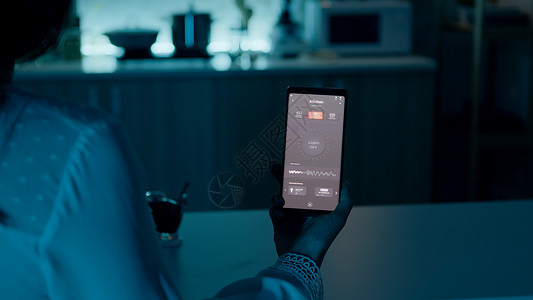 坐在家里的女人拿着智能手机的自动化照明系统灯光房间创新经济互联网安全厨房屏幕房子监控移动的高清图片素材