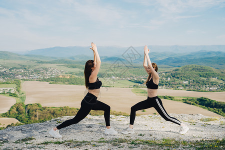 瑜伽图两个女孩在悬崖上玩运动 天性瑜伽青菜腰部蓝色蒸汽树木空气石头训练女孩山脉背景