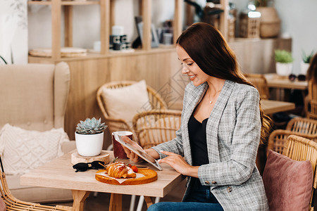 一个女孩坐在咖啡馆里看着平板电脑 一个女孩在咖啡馆里微笑 远程工作女士长发药片早餐黑发玻璃香味享受强人杯子年轻的高清图片素材
