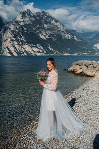 蓝发蓝礼服女孩一名女性在意大利一座山和湖的背景下被拍到照片 TorboleTorbole 在Lake Garda湖的堤岸上行走蓝色山脉白色公主背景