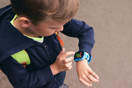 语音手表可穿戴儿童婴儿智能手表通过触摸屏和语音服务呼叫妈妈和位置跟踪 蓝色多色电子小工具 带儿童橡胶腕带 特写有拷贝空间的男孩 学校的时背景