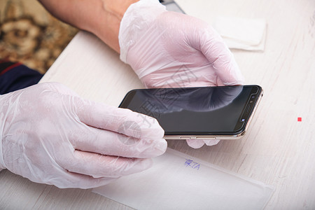 一个戴橡皮手套的男人拿着一个电话 他用屏幕上的新玻璃杯修理了一部电话木板高清图片素材