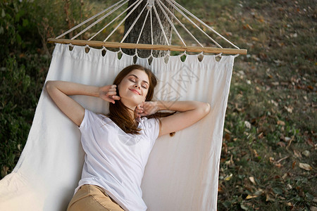 快乐的女人躺在一个吊床露天度假暑假的户外露台女士假期阴影青少年旅行女孩休息室女性后院太阳高清图片素材