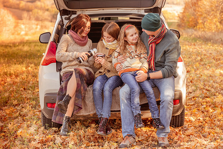 十月女孩家庭坐在汽车后备箱中森林快乐树干叶子环境女孩父母女学生树叶姐姐背景