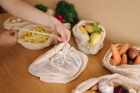 水果袋女人的手 特写一个可再用杂货袋 把蔬菜放在家里桌子上的菜子生态烹饪送货互联网工艺回收厨房自然棉布市场背景