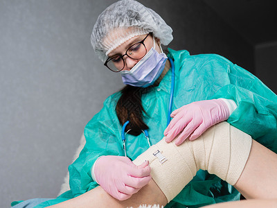 白色石膏一名身戴医疗手套的年轻护士在病人的腿和膝盖上贴了弹性绷带 这是物理治疗室背景