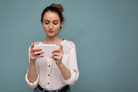 身着便衣的美丽年轻女子透过手机看移动屏幕 在互联网上背景冲浪时与外界隔绝地站立女士创造力电话技术神器思考思维女性衬衫互联网背景图片