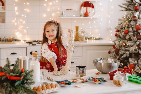 新年厨房红围裙的小女孩 为圣诞饼干准备了面粉 来做圣诞饼干团队房子助手女儿父母面团喜悦厨师价值观桌子背景图片