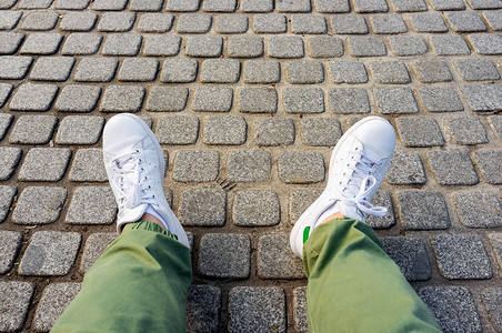 在cobblestone人行道上穿绿色长裤和白色运动鞋的男子腿质地高清图片素材