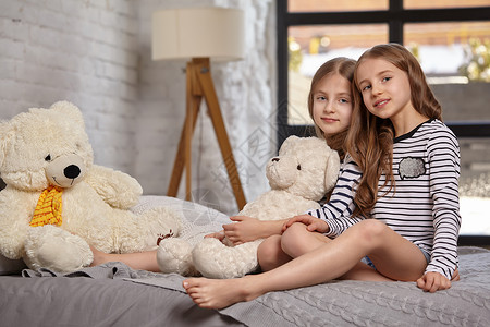 房间里两个小姐妹坐在床上的画面乐趣卧室女儿快乐金发寝具休息喜悦枕头孩子们健康高清图片素材