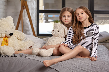 房间里两个小姐妹坐在床上的画面女性枕头金发女郎姐姐乐趣卧室快乐喜悦孩子们漂亮的高清图片素材