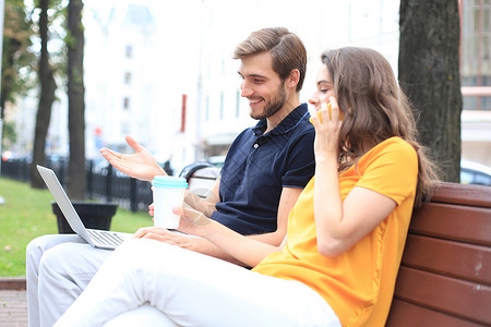 年轻夫妇在户外坐在长椅上时使用笔记本电脑电话触摸屏房间屏幕女士手机技术女朋友喜悦微笑空的高清图片素材