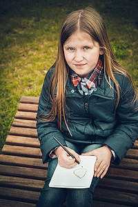 梦娃素材春春时一位金发女学生 坐在公园的木板凳上写了一封信背景