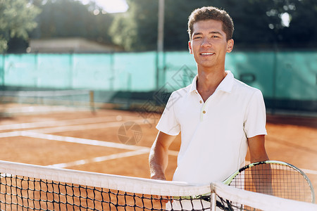 在网球场站着电击的年轻混种男子网球运动员教练男人人手老师法庭运动红土混血玩家背景图片