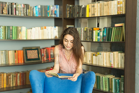 人 教育和知识概念     图书馆中的妇女读物书阅读学生家具女孩女学生专注女性成人蓝色享受漂亮的高清图片素材