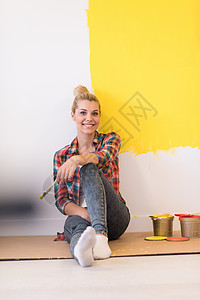 微笑墙坐在地板上的年轻女画家画笔金发房子工作维修女士滚筒女郎公寓微笑背景