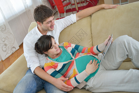 在家中使用平板电脑的怀孕夫妇男人药片微笑沙发房子电子书女士父亲母亲房间软垫高清图片素材