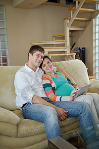 在家中使用平板电脑的怀孕夫妇房子女孩药片软垫沙发技术房间母亲母性父母快乐的高清图片素材