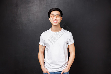 戴眼镜的亚洲年轻男子的肖像站在黑色背景的白色休闲衬衫上 友好的微笑 表达快乐的热情情绪 大学毕业后与朋友一起闲逛教育高清图片素材