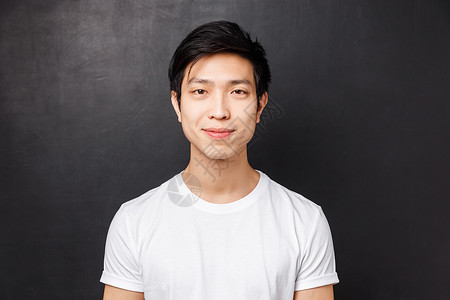 穿着白色 T 恤 面带微笑的亚洲年轻男模的特写 看着镜头 咧着嘴笑 站在黑色背景上 人们的情感和生活方式的概念种族高清图片素材