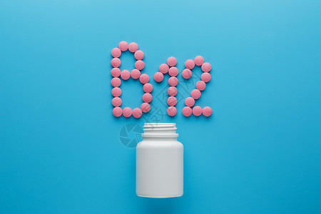 粉色药片粉色药丸 以字母B12的形状 在蓝色背景上 从白色罐头溢出标签治疗药物瓶子地面包装食物剂量塑料木头背景