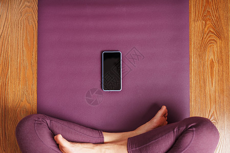 瑜伽视频课一名女孩在家里用智能手机和移动应用程序在长毯地毯上做瑜伽和冥想活力地面呼吸互联网教程训练三脚架视频女士平衡背景